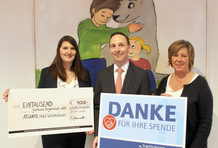 Drei Personen halten einen Scheck und ein Dankesschild für eine Spende im ATLANTIC Hotel Wilhelmshaven.