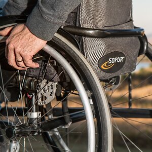 Close-up of a hand touching the wheel of an outdoor wheelchair.