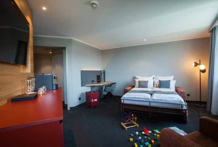 Bright hotel room with double bed, desk, toys on the floor and modern decor at the ATLANTIC Hotel Airport Bremen.