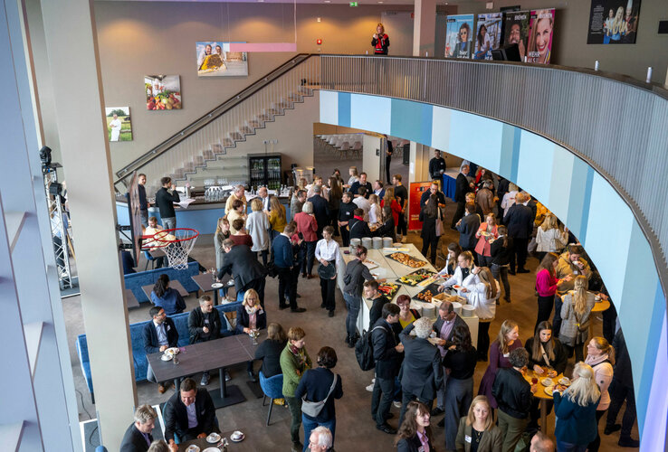 Menschen versammeln sich in einem modernen, lichtdurchfluteten Hotelraum mit Buffet und Sitzgelegenheiten.