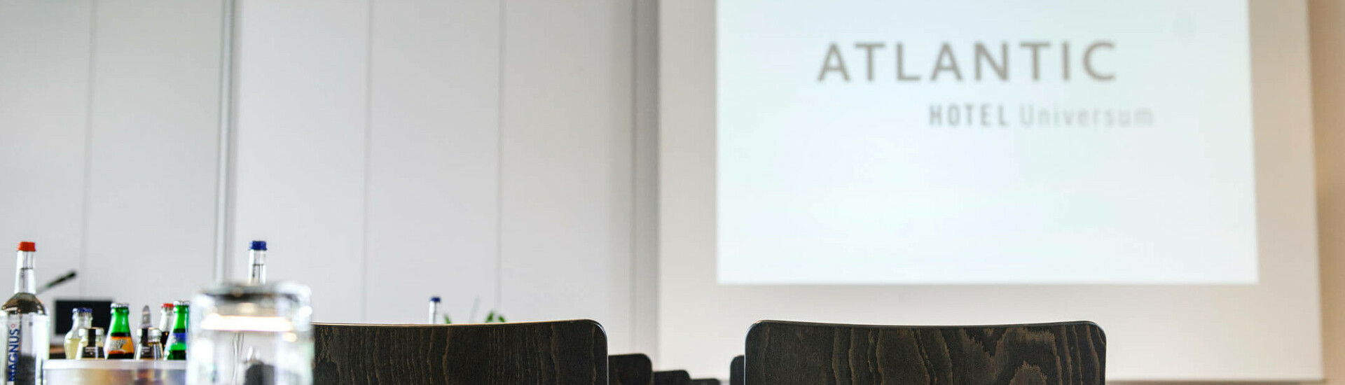 Tagungsraum Saal 1 Parlamentarisch | Conference Center im ATLANTIC Hotel Universum in Bremen Konferenzraum im ATLANTIC Hotel Universum mit Stühlen, Tischen und Getränken, Blick auf eine Projektionsleinwand.