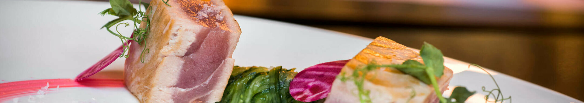 Gourmet dish with tender fish, decorated with beet slices and herbs on an elegant white plate.