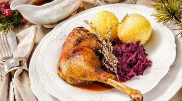 Festliches Gericht mit Entenkeule, Rotkohl und Kartoffelklößen auf weißem Teller, dekoriert mit Kräutern.