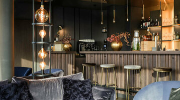 Elegante Hotelbar mit blauen Samtmöbeln, stilvollen Lampen und gut bestückter Theke im ATLANTIC Hotel Münster.