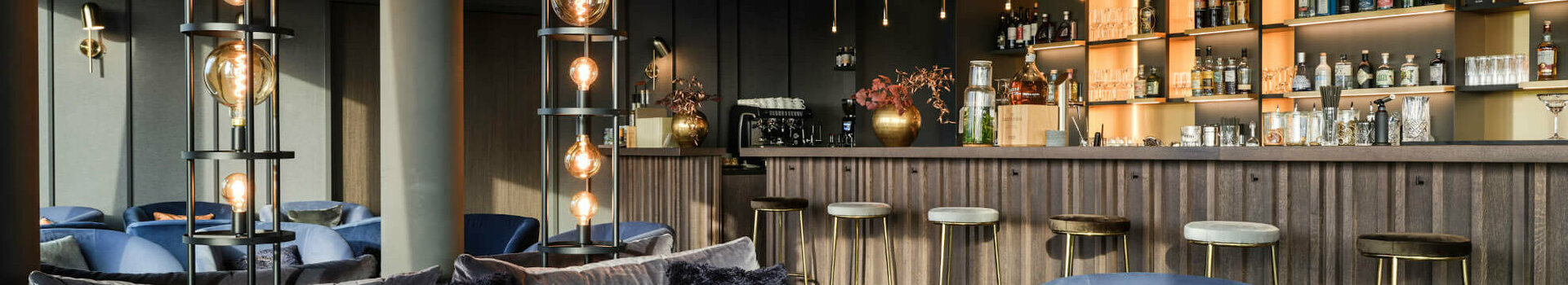 Bar im ATLANTIC Hotel Münster Elegante Hotelbar mit blauen Samtmöbeln, stilvollen Lampen und gut bestückter Theke im ATLANTIC Hotel Münster.