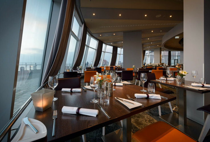Modernes Restaurant mit gedeckten Tischen, großen Fenstern und Blick auf die Promenade im ATLANTIC Hotel Sail City.