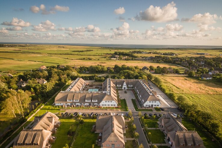 Aerial view of a hotel with courtyard, surrounded by green fields and scattered buildings under a blue sky.