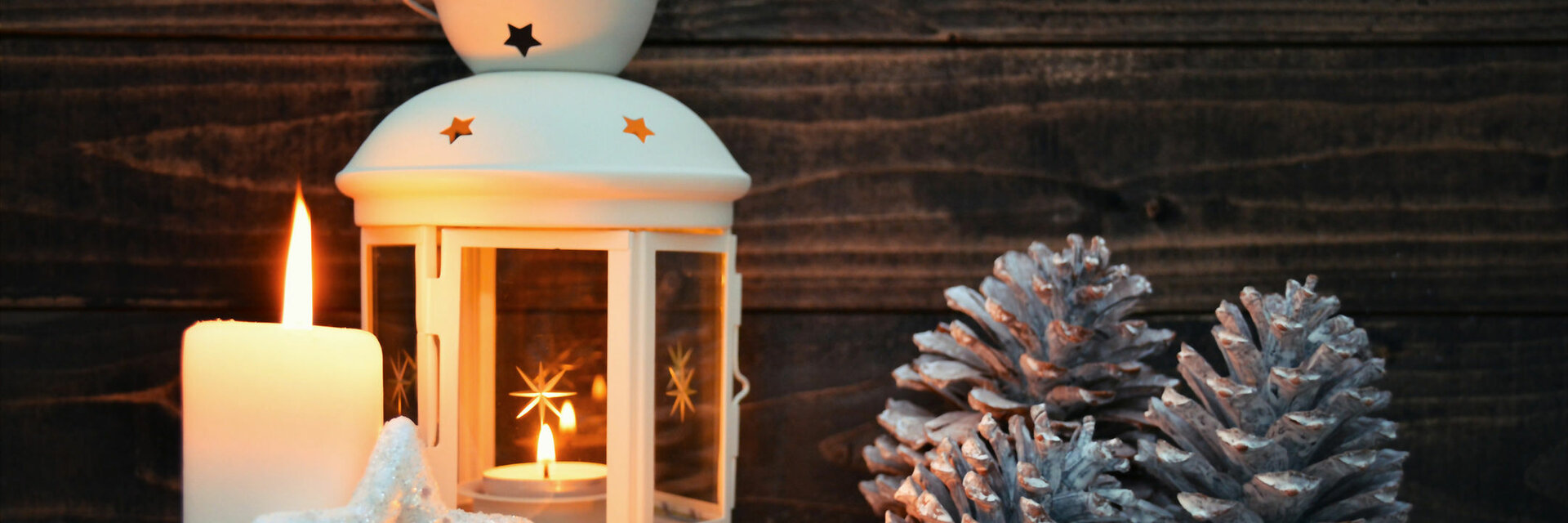 White lantern with candles, pine cones and Christmas baubles on a snow-covered wooden background. Atmospheric winter decoration.