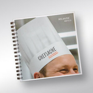 Chef in white cap with "Chefsache" inscription, smiling, part of the ATLANTIC Hotel.