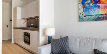 Modern hotel room view with kitchenette, grey sofa, stylish lamp and colorful mural.