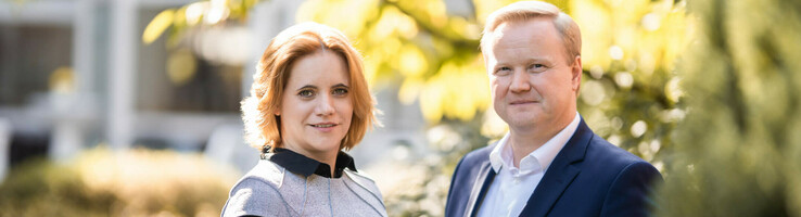 Ein Mann und eine Frau stehen lächelnd im Garten des ATLANTIC Hotel Landgut Horn Bremen.