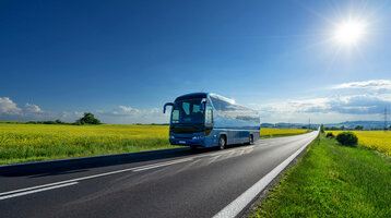 Group tours ATLANTIC Hotel Vegesack  Coach on a country road, surrounded by yellow fields under a blue sky with sun.