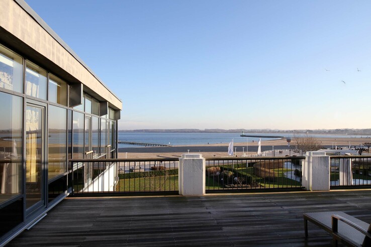 Blick von der Hotelterrasse auf Strand und Meer, mit blauem Himmel und Promenade im ATLANTIC Grand Hotel Travemünde.