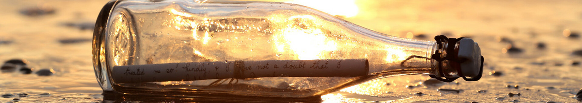 ATLANTIC Grand Hotel Travemünde Header Contacts A message in a bottle lies on the beach at sunset, the paper is visible through the glass.