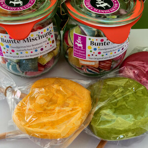 Bonbons aus der Bremer Bonbon Manufaktur Bunte Bonbons in Gläsern und große Lutscher in Orange, Grün und Rot, verpackt in durchsichtiger Folie.