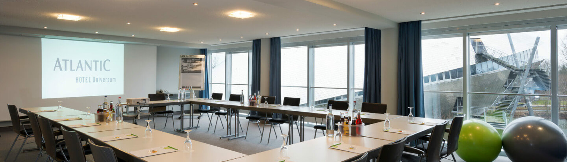 Tagungsraum Conrad Röntgen im ATLANTIC Hotel Universum Bremen Heller Konferenzraum im ATLANTIC Hotel Universum mit U-förmiger Tischanordnung, Leinwand und großen Fenstern.