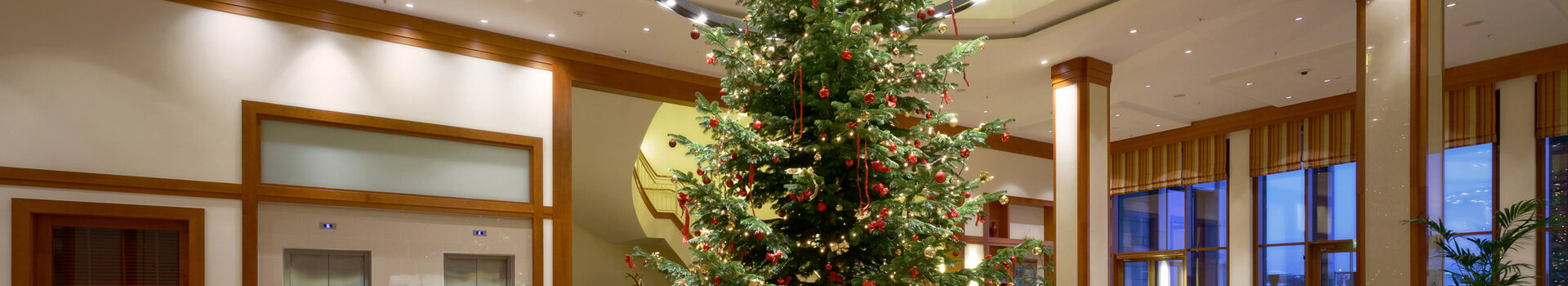 ATLANTIC Hotel Wilhelmshaven | Advent season Elegant hotel lobby with large, decorated Christmas tree, surrounded by seating areas and modern lighting.