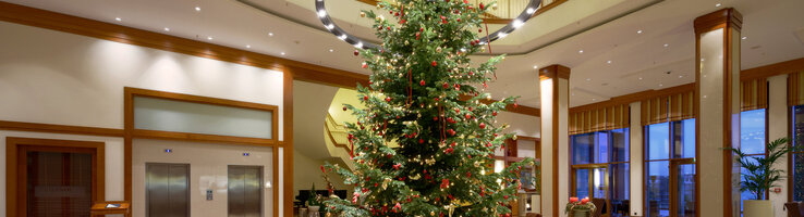 Elegante Hotellobby mit großem, geschmücktem Weihnachtsbaum, umgeben von Sitzgruppen und moderner Beleuchtung.