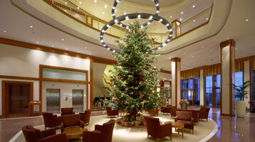 Elegante Hotellobby mit großem, geschmücktem Weihnachtsbaum, umgeben von Sitzgruppen und moderner Beleuchtung.