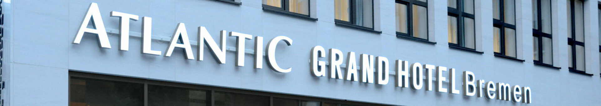 Eingang des ATLANTIC Grand Hotel Bremen mit moderner Glasfassade und beleuchtetem Hotellogo.