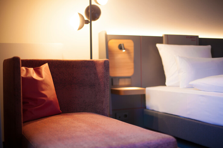 Modern hotel room with cozy armchair, cushions, bed and stylish lighting at the ATLANTIC Hotel Airport Bremen.