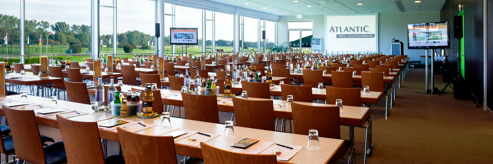 Moderner Konferenzraum im ATLANTIC Hotel Galopprennbahn Bremen mit Tischen, Stühlen und Blick auf die Rennbahn.
