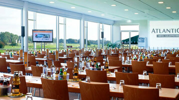Modern conference room at the ATLANTIC Hotel Galopprennbahn Bremen with tables, chairs and a view of the racecourse.