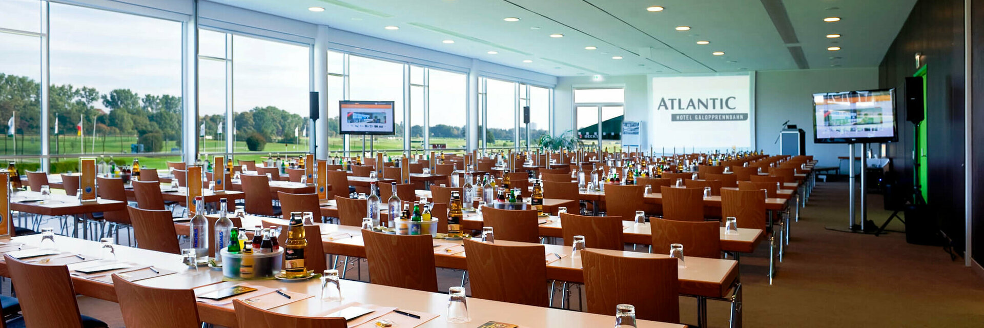 Modern conference room at the ATLANTIC Hotel Galopprennbahn Bremen with tables, chairs and a view of the racecourse.