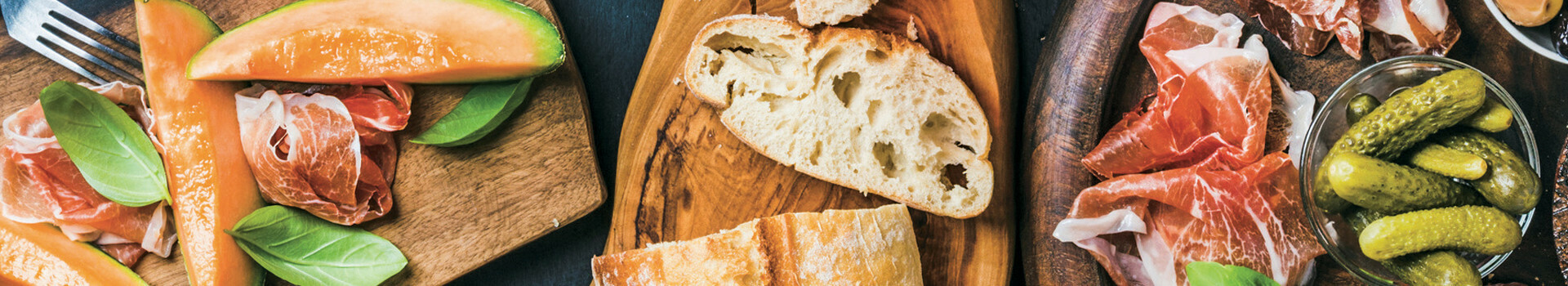 Mediterranean dinner at the restaurant DERBY Various antipasti with melon, ham, bread, gherkins and olives served on a wooden board.