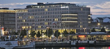 Modern hotel building on the waterfront at dusk, illuminated with reflecting light in the river.