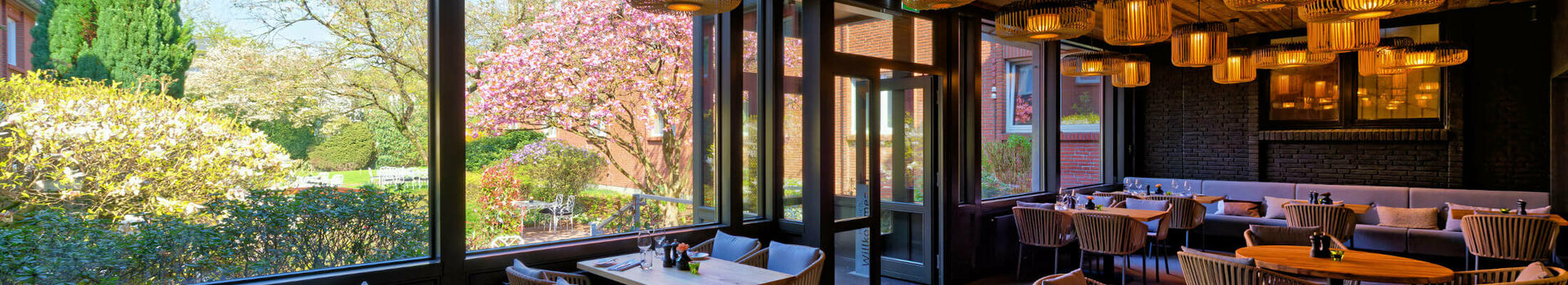 Cozy restaurant with wooden tables and ceilings, large windows with garden views and stylish lamps.