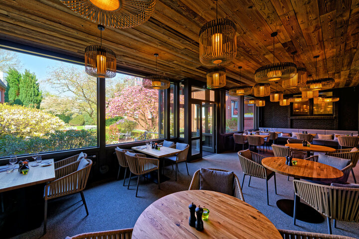 Winter garden at the ATLANTIC Hotel Landgut Horn Cozy restaurant with wooden tables and ceilings, large windows with garden views and stylish lamps.