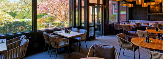 Gemütliches Restaurant mit Holztischen und -decken, großen Fenstern mit Gartenblick und stilvollen Lampen.