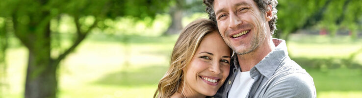 Lächelndes Paar umarmt sich im grünen Park vor dem ATLANTIC Hotel Universum in Bremen.