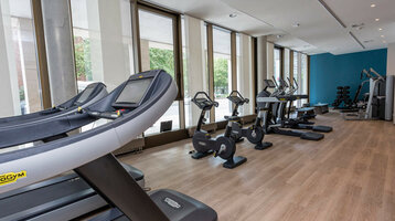 Modern fitness room in the ATLANTIC Grand Hotel Bremen with treadmills, bicycles and weight machines, bright window front.