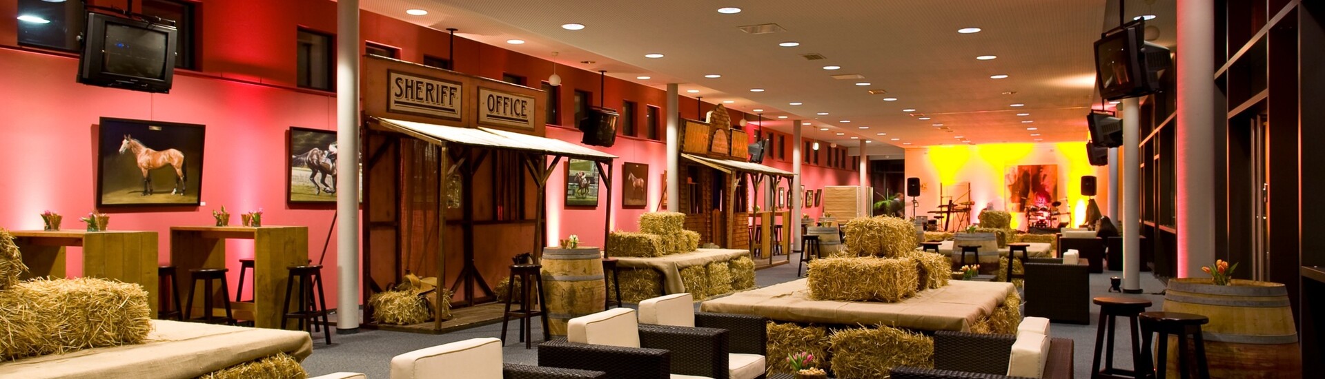 Modern lounge area in western style with straw bales, wooden furniture and pictures of horses, atmospheric lighting.