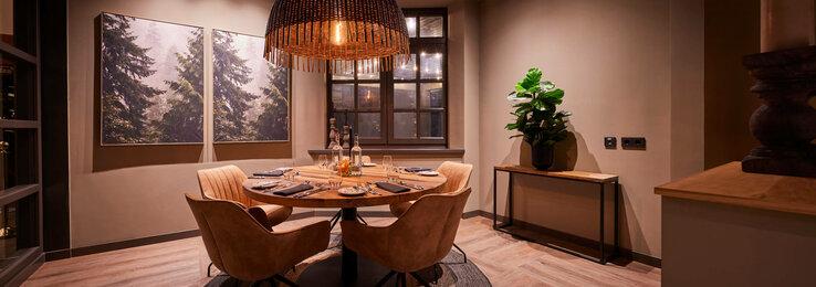 Corner im Restaurant Chalet im ATLANTIC Hotel Landgut Horn Bremen  Gemütlicher Essbereich im ATLANTIC Hotel Landgut Horn, mit Holztisch, vier Stühlen, großer Lampe und Naturbildern an der Wand.