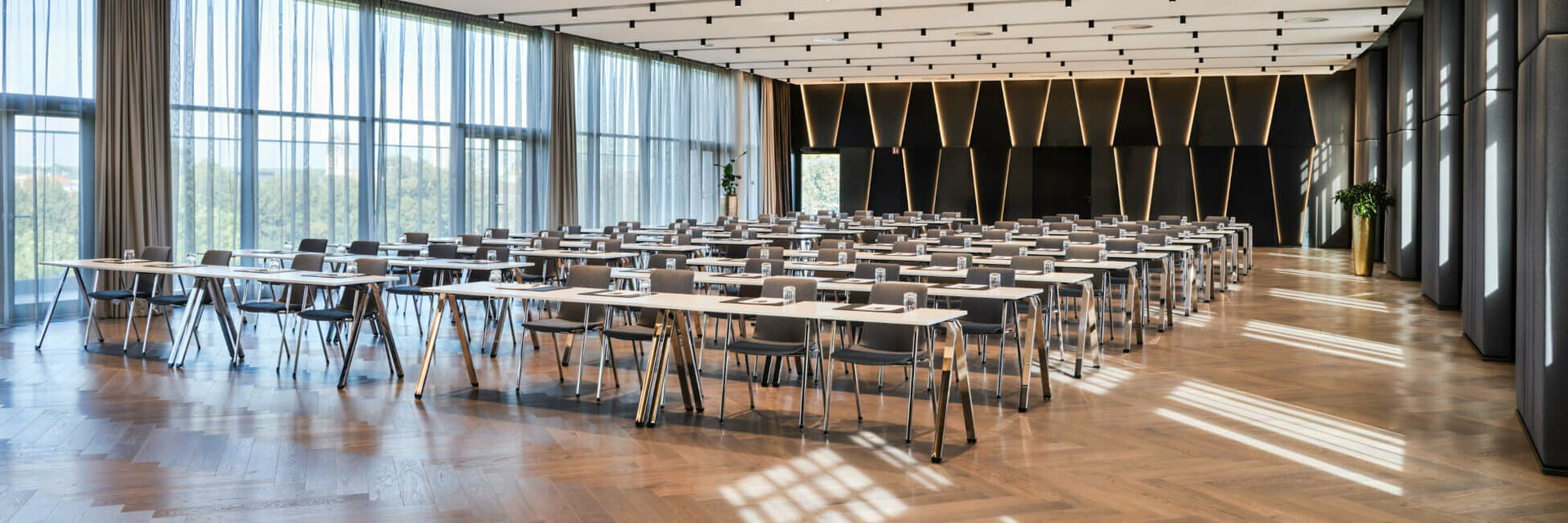Modern conference room at the ATLANTIC Hotel Münster with rows of tables, chairs and large windows.
