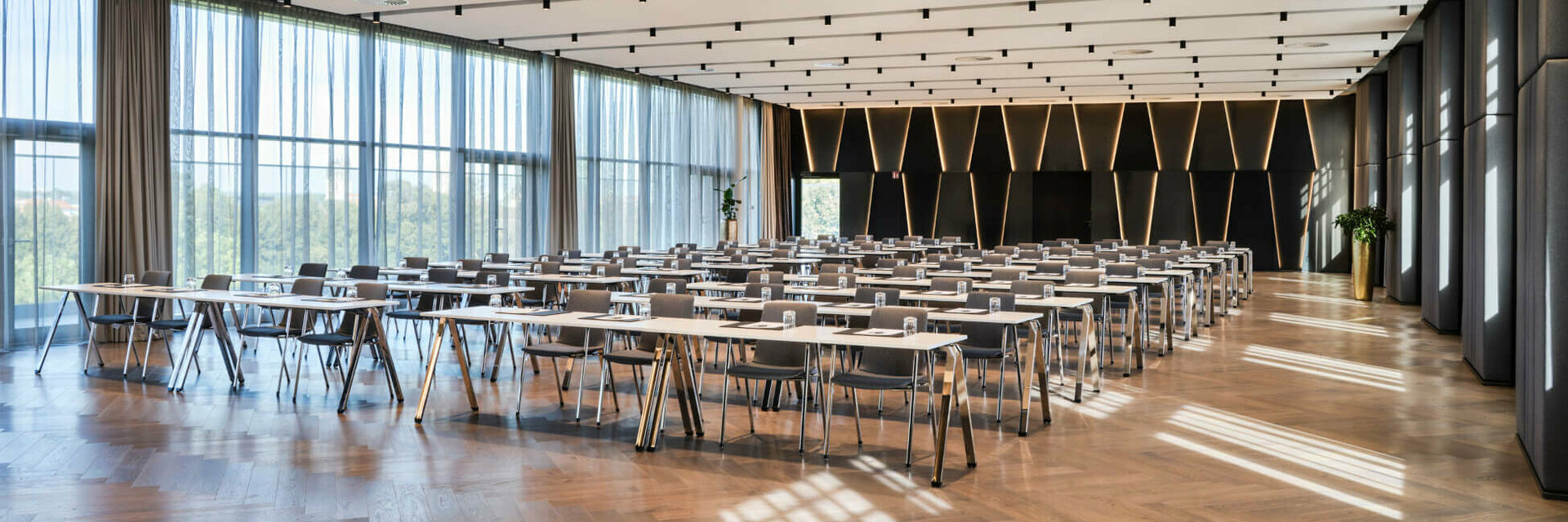 Moderner Konferenzraum im ATLANTIC Hotel Münster mit Reihen von Tischen, Stühlen und großen Fenstern.