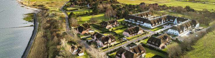 Severins Resort & Spa Sylt Aussenaufnahme Luftaufnahme eines Hotels mit Reetdachhäusern, umgeben von grünen Wiesen und nahe der Küste.