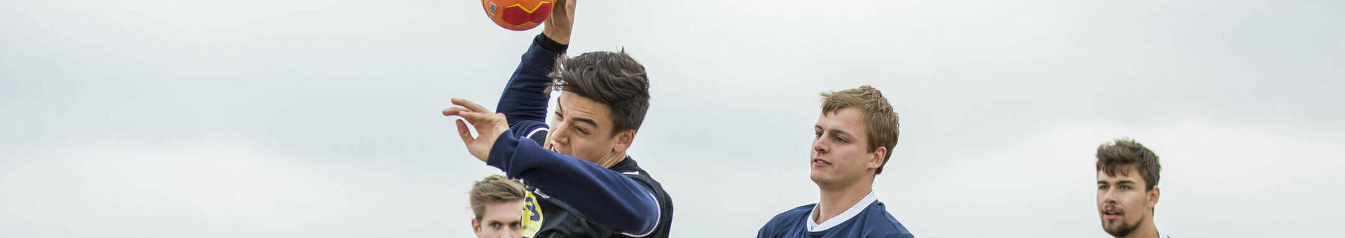 Gruppe junger Männer spielt Beachhandball am Strand, dynamische Szene mit Spielern in Aktion.