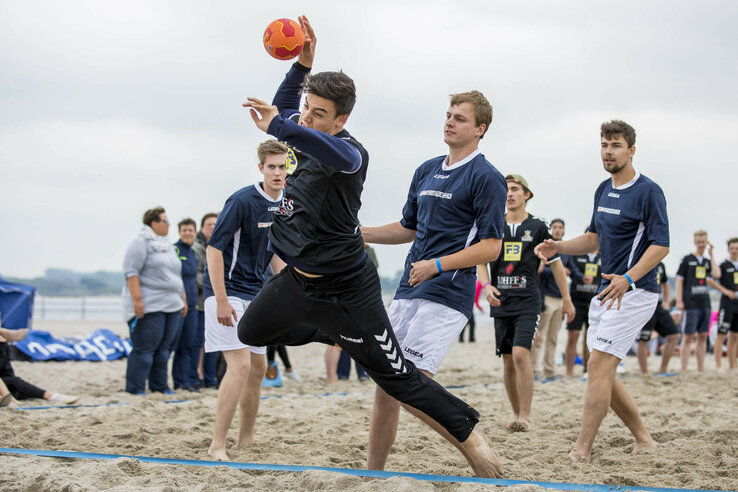 Gruppe junger Männer spielt Beachhandball am Strand, dynamische Szene mit Spielern in Aktion.