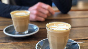 Zwei Flat White Kaffee mit Untertassen auf einem Holztisch.