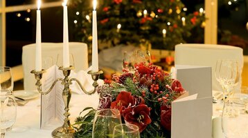 Festively laid table with candlesticks, red flowers and Christmas tree in the background.