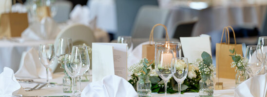 Eleganter, festlich gedeckter Tisch mit weißen Tischdecken, Blumenarrangements und Kerzen im ATLANTIC Hotel Landgut Horn Bremen.