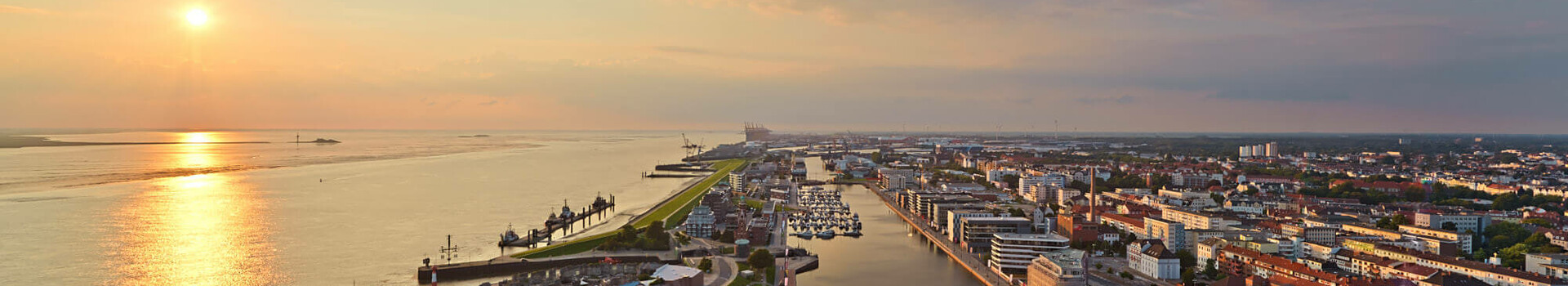 Blick auf Bremerhaven vom ATLANTIC Hotel Sail City bei Sonnenuntergang, mit Hafen, Fluss und Stadtpanorama.