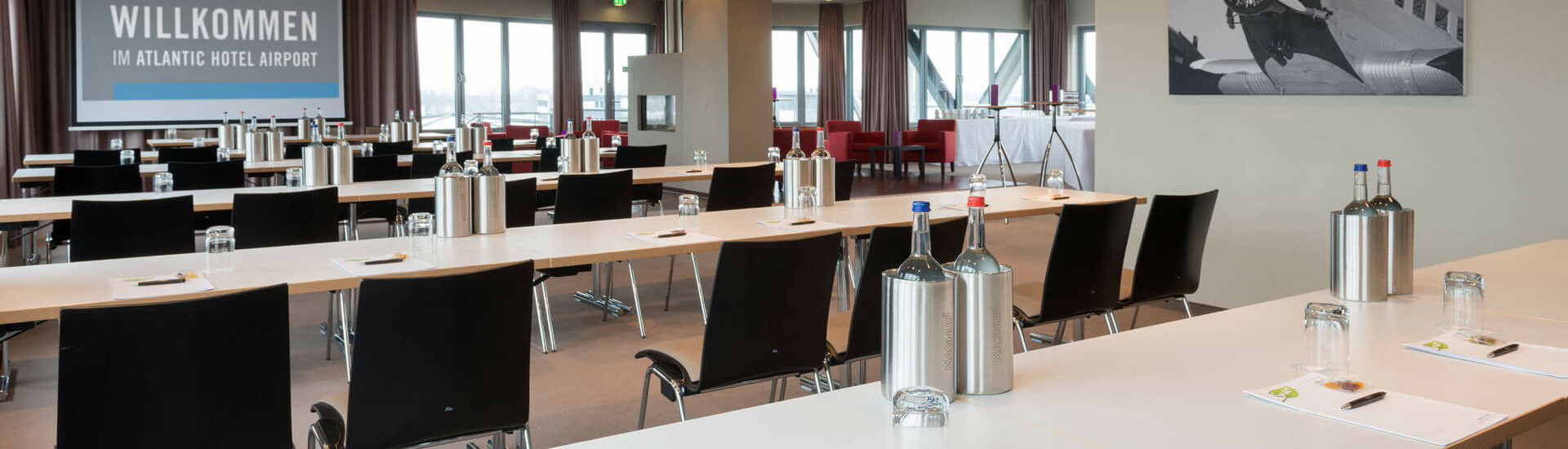 Modern conference room at the ATLANTIC Hotel Airport Bremen with tables, chairs and presentation screen.