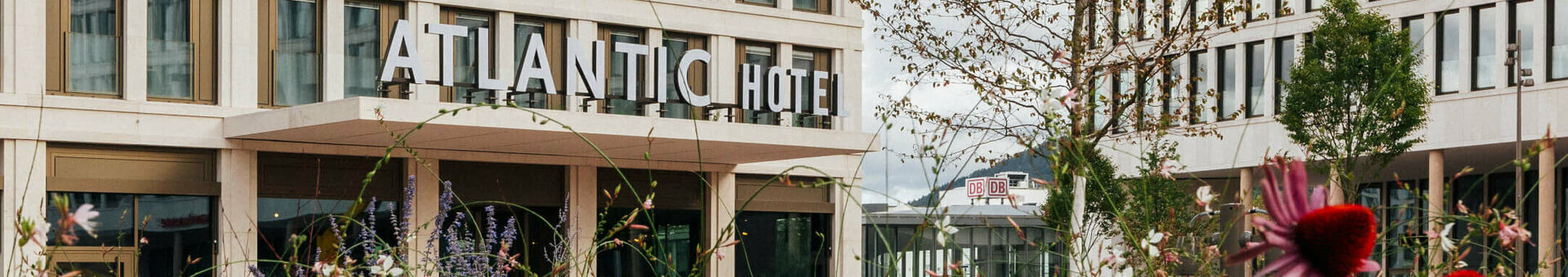 ATLANTIC Hotel Heidelberg Hochzeiten feiern Außenansicht des ATLANTIC Hotel Heidelberg mit modernen Gebäuden und blühenden Blumen im Vordergrund.