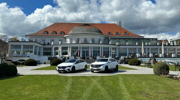 Das ATLANTIC Grand Hotel Travemünde mit rotem Dach, grüner Wiese und zwei weißen Autos im Vordergrund.