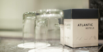 Zwei umgedrehte Gläser auf Untersetzern neben einer ATLANTIC Hotels Box auf einer glänzenden Oberfläche.